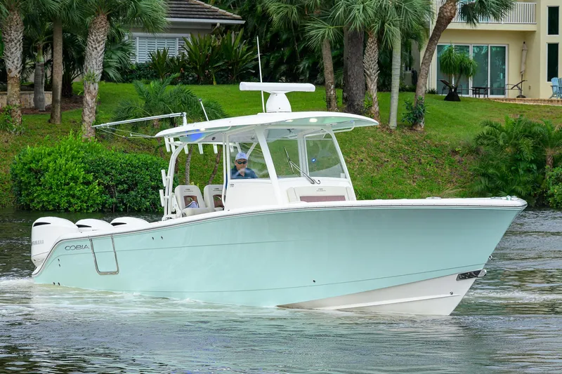 Slide: The Image of 2020 Cobia 350 CC boat cruising on a scenic waterway with lush greenery. - 2