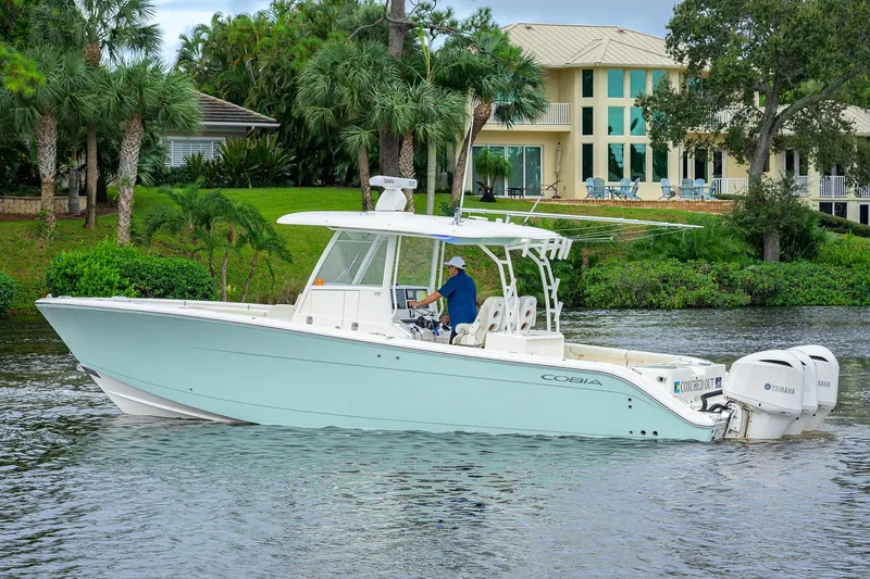 Slide: The Image of 2020 Cobia 350 CC boat cruising on a scenic waterway near a luxurious waterfront home. - 6