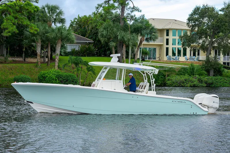 Slide: The Image of 2020 Cobia 350 CC boat cruising on a scenic waterway near a luxurious waterfront home. - 7