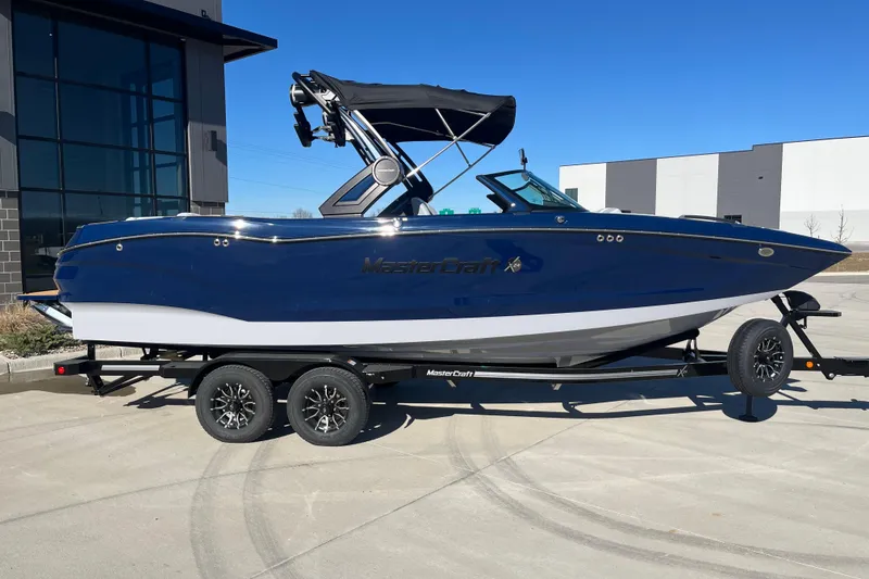 Slide: The Image of 2025 MasterCraft X24 boat on trailer, blue and white design, parked outdoors. - 2