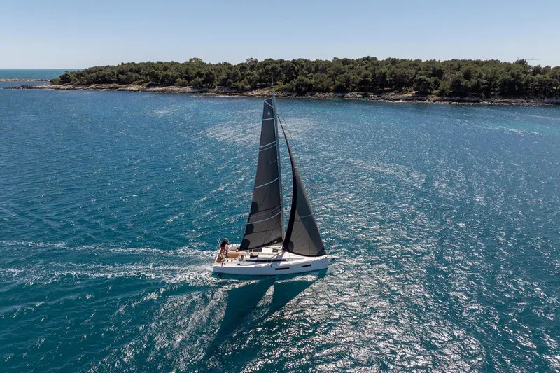 Slide: The Image of Sailing yacht Jeanneau Sun Odyssey 350 (2026) cruising on clear blue waters near a forested coastline. - 4
