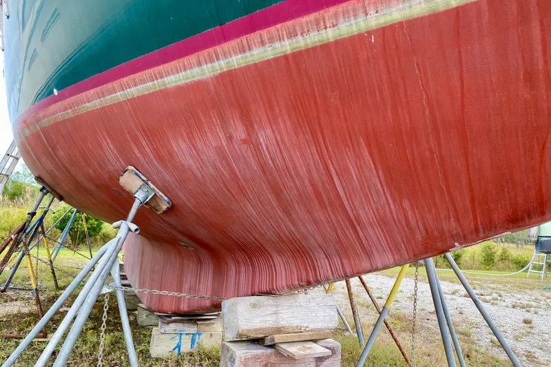 Slide: The Image of 1983 Liberty 38 Cutter sailboat hull on stands, showing weathered red paint. - 44