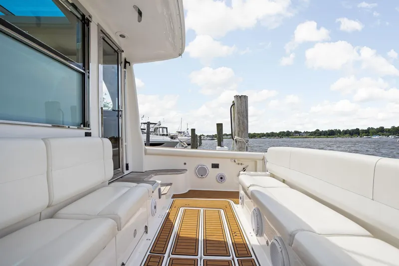 Slide: The Image of 2003 Tiara Yachts 5200 Sovran deck with white seating and wooden flooring, docked by the water. - 3