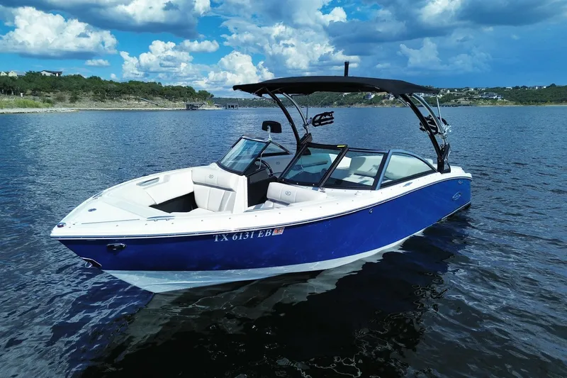 Slide: The Image of 2018 Cobalt CS23 Surf boat on a scenic lake under a cloudy sky. - 0