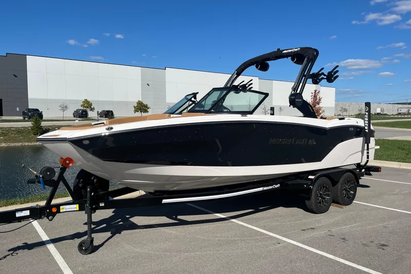The Image of 2025 MasterCraft NXT23 boat on trailer in parking lot, sunny day. - 1