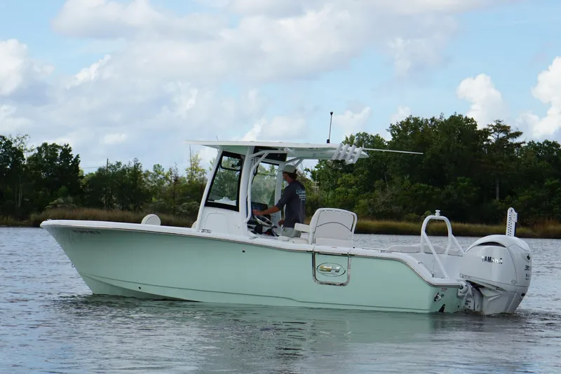 Slide: The Image of 2024 Sea Hunt Ultra 255 SE boat on calm water, surrounded by trees and cloudy sky. - 16