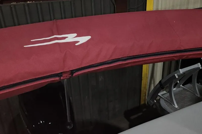Slide: The Image of 2022 Bennington 198SL boat with maroon canopy and logo, partially visible in storage. - 15