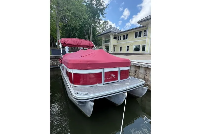 Slide: The Image of 2022 Bennington 198SL pontoon boat with red cover docked by a lakeside building. - 5