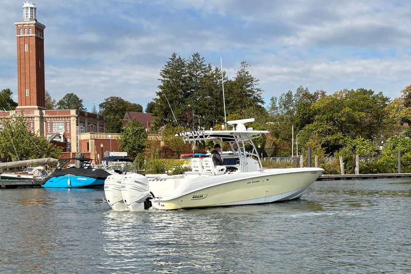 Slide: The Image of 2008 Boston Whaler 320 Outrage boat cruising near a scenic waterfront with a tall building. - 4