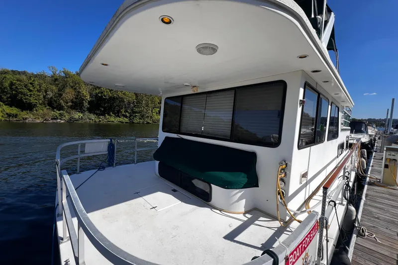 Slide: The Image of 1994 Gibson 44 Classic houseboat docked by a scenic river under a clear blue sky. - 2