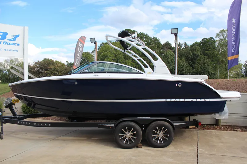 Slide: The Image of 2026 Four Winns H2 Freedom boat on trailer, displayed outdoors with flags and trees. - 6