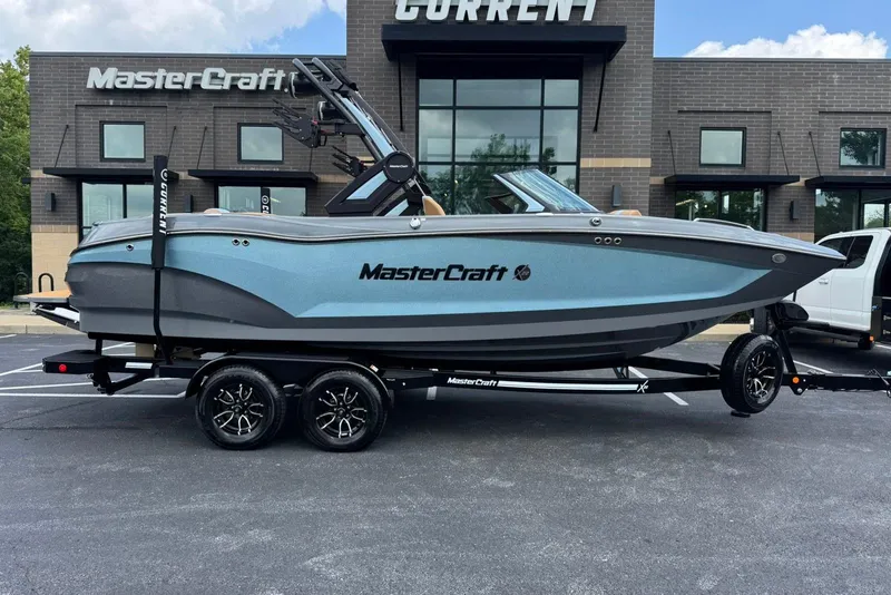 Slide: The Image of 2025 MasterCraft X22 boat on trailer, parked outside dealership, side view. - 2