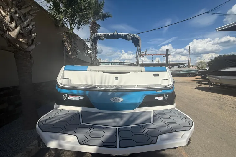 Slide: The Image of 2021 MasterCraft NXT24 boat with blue and white design, parked outdoors under a clear sky. - 6