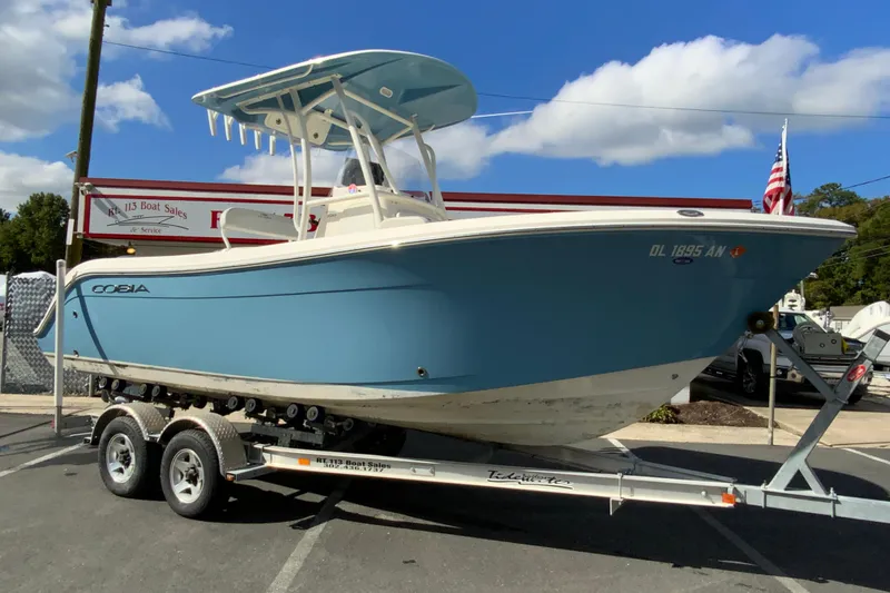 Slide: The Image of 2021 Cobia 220 Center Console boat on trailer at dealership, under clear sky. - 2
