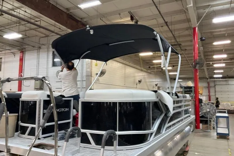 Slide: The Image of 2026 Bennington 22 SSRSF pontoon boat in a warehouse, with a person adjusting the canopy. - 7