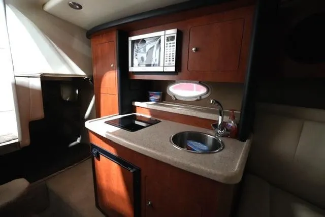 Slide: The Image of 2007 Rinker Fiesta Vee 280 boat interior with kitchenette, featuring microwave, sink, and compact fridge. - 28