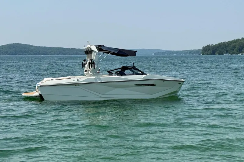 Slide: The Image of 2025 Nautique Super Air Nautique G23 boat on a serene lake with lush green surroundings. - 2