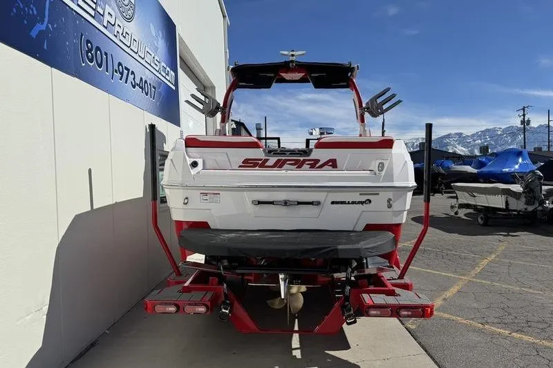 Slide: The Image of 2024 Supra SL 575 boat, rear view, parked outdoors with mountains in background. - 2