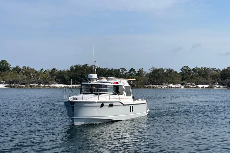 Slide: The Image of 2023 Ranger Tugs R-25 boat cruising on a calm lake with forested shoreline. - 2