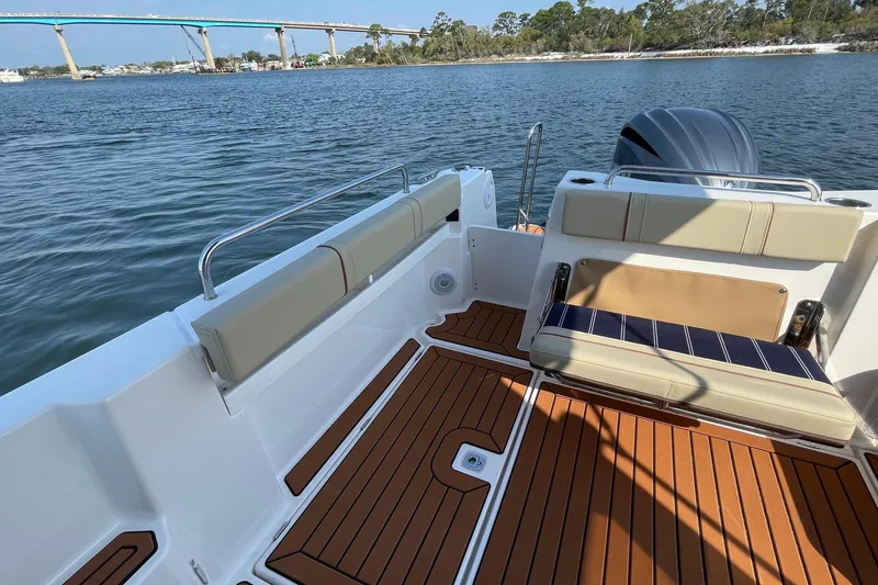 Slide: The Image of 2023 Ranger Tugs R-25 boat interior with cushioned seating and wooden deck, near a scenic bridge. - 22