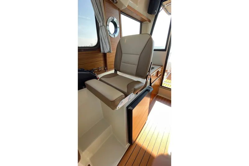 Slide: The Image of Captain's seat in 2023 Ranger Tugs R-25 boat, featuring wood accents and window view. - 33