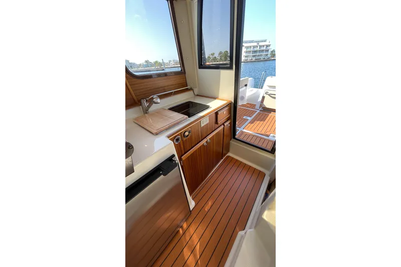 Slide: The Image of 2023 Ranger Tugs R-25 interior with wooden cabinetry, sink, and outdoor view. - 36