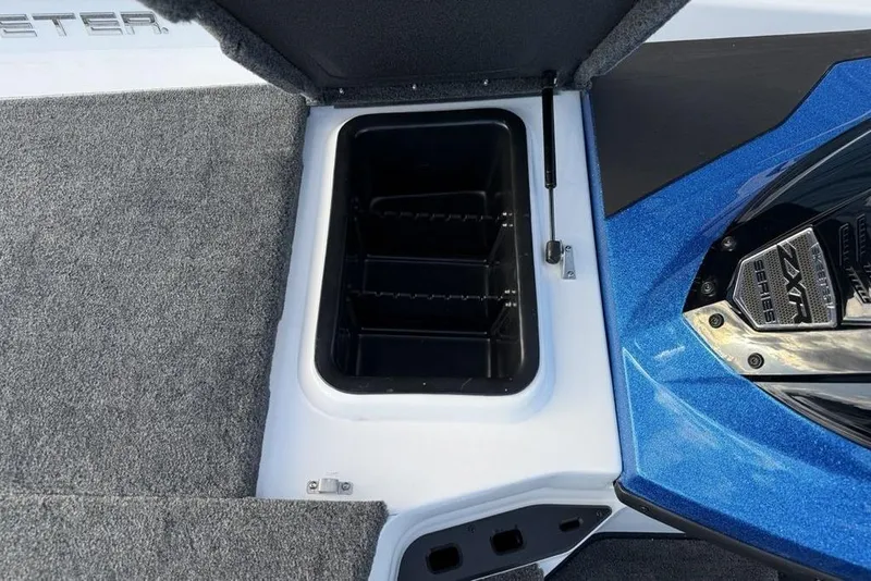 Slide: The Image of Open storage compartment in 2026 Skeeter ZXR19 SE boat, featuring carpeted interior and blue exterior. - 13