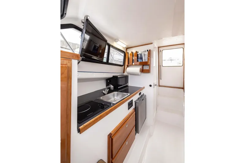 Slide: The Image of 2023 Skipjack 26 Flybridge interior with kitchenette, sink, stove, and TV. - 32