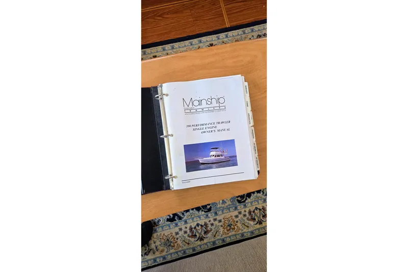 Slide: The Image of Manual for 2000 Mainship 390 Trawler on wooden table, open binder view. - 24