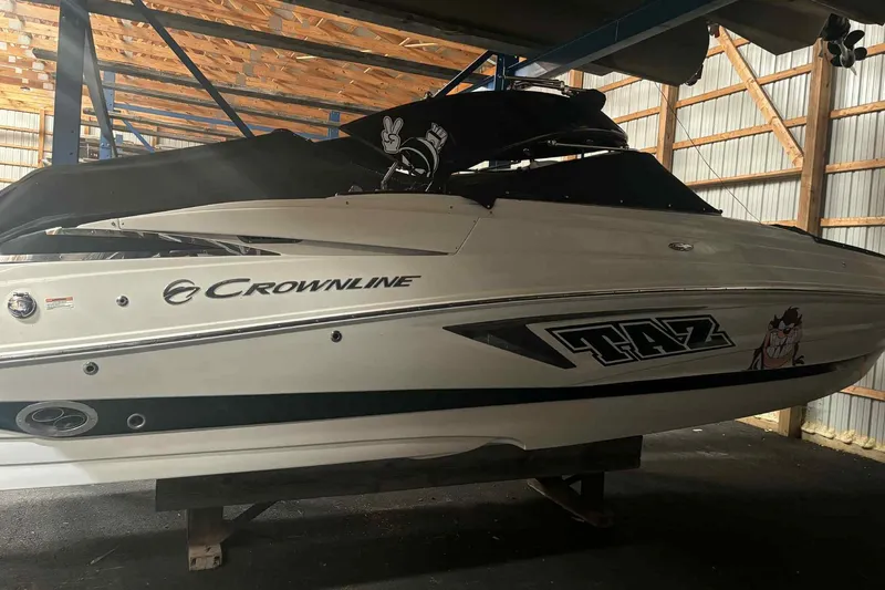 The Image of 2021 Crownline 290 SS boat on trailer under wooden shelter by a lake. - 0