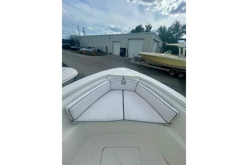 Slide: The Image of 2006 Triton 225 CC boat with white cushioned seating, parked near a warehouse. - 3