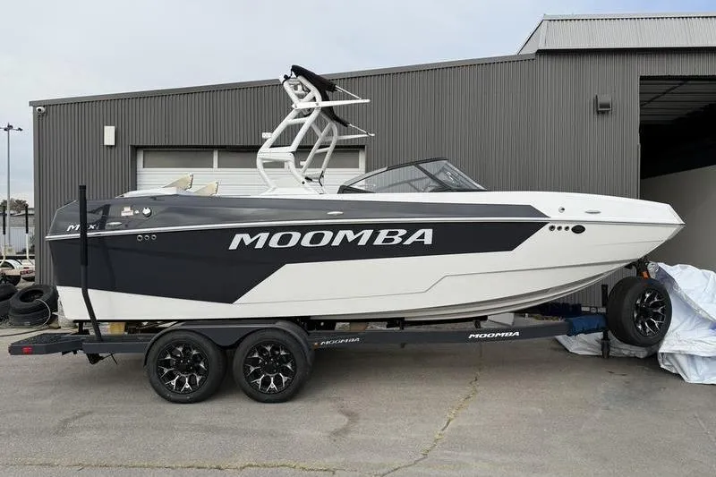 Slide: The Image of 2025 Moomba Max boat on trailer, parked outside a gray industrial building. - 0