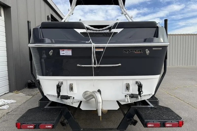 Slide: The Image of 2025 Moomba Max boat rear view on trailer, parked near industrial building. - 2