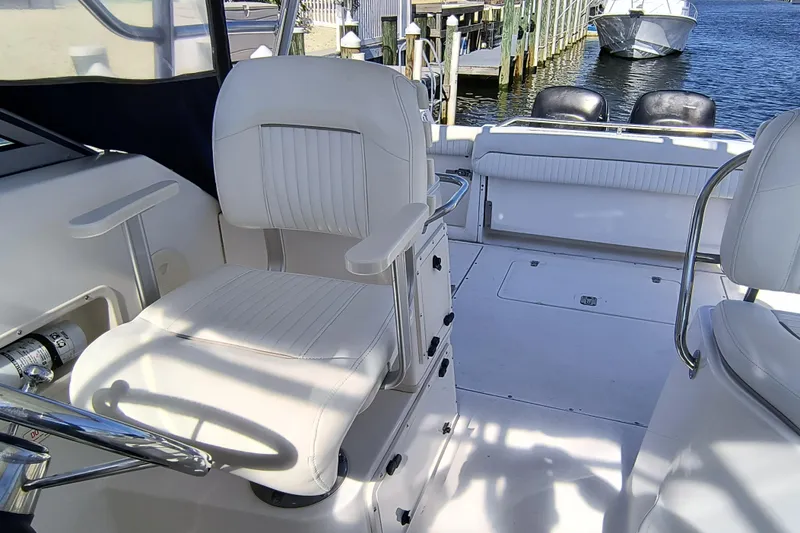 Slide: The Image of 2002 Boston Whaler 295 Conquest interior with white seating and steering wheel, docked by water. - 8