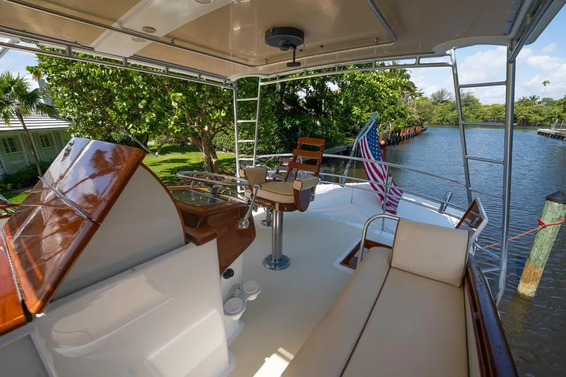 Slide: The Image of 1970 Rybovich 54 yacht deck with seating, helm, and American flag by a scenic river. - 14