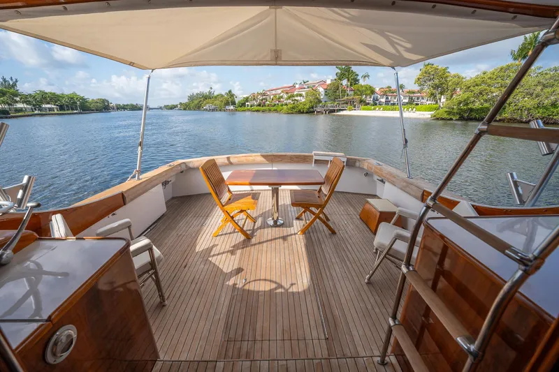 Slide: The Image of 1970 Rybovich 54 yacht deck with wooden chairs and table, overlooking serene waterfront scenery. - 16