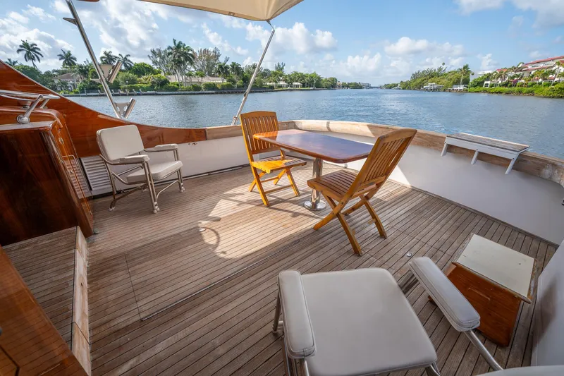Slide: The Image of 1970 Rybovich 54 yacht deck with wooden chairs, table, and scenic waterfront view. - 17