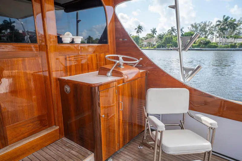 Slide: The Image of 1970 Rybovich 54 yacht interior with polished wood, steering wheel, and white chair by the water. - 19