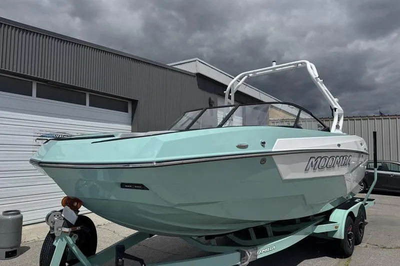 Slide: The Image of 2025 Moomba Max boat in mint green on trailer, parked outside industrial building. - 2