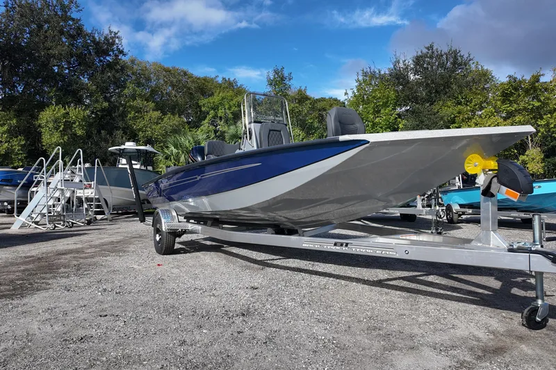 Slide: The Image of 2026 Xpress H20B Bay boat on trailer, parked outdoors with trees in background. - 2
