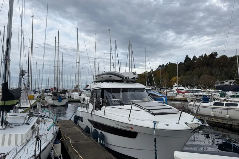 Slide: The Image of 2019 Jeanneau NC 895 docked in a marina, surrounded by sailboats under cloudy skies. - 26