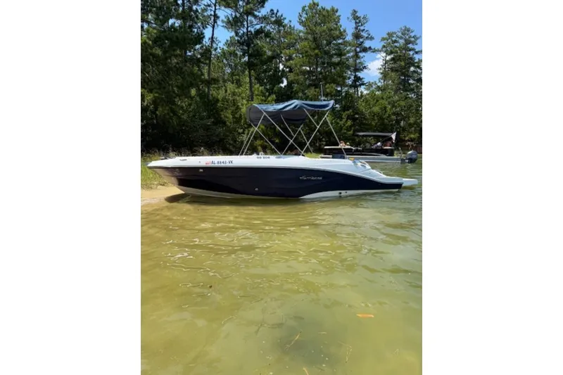 Slide: The Image of 2021 Hurricane SunDeck Sport 205 IO boat docked by a forested shoreline. - 17