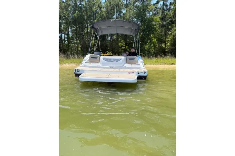 Slide: The Image of 2021 Hurricane SunDeck Sport 205 IO boat docked near a forested shoreline. - 19