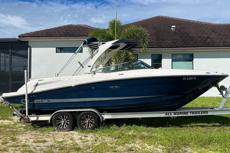 Slide: The Image of 2012 Sea Ray 250 SLX boat on trailer, parked near a house with palm tree. - 0