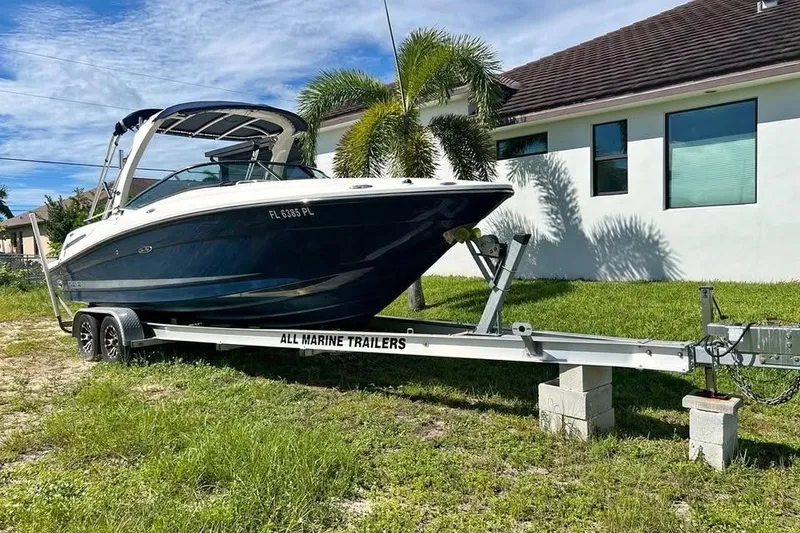 Slide: The Image of 2012 Sea Ray 250 SLX boat on trailer, parked beside a house with palm trees. - 1
