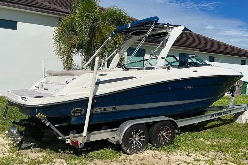 Slide: The Image of 2012 Sea Ray 250 SLX boat on trailer, parked near a house with palm trees. - 2