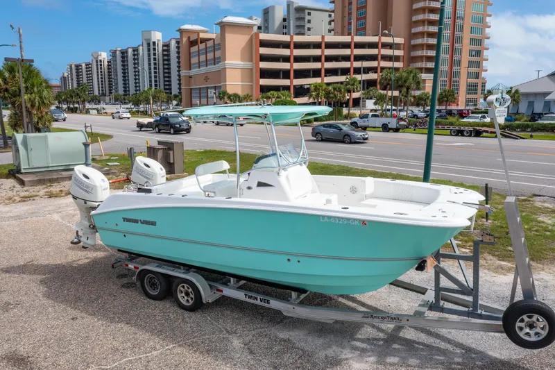 Slide: The Image of 2019 Twin Vee 240 GFX CC boat on trailer, parked near coastal road with buildings. - 0