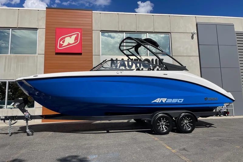 The Image of 2025 Yamaha Boats AR250 in blue, displayed on a trailer outside a dealership. - 1