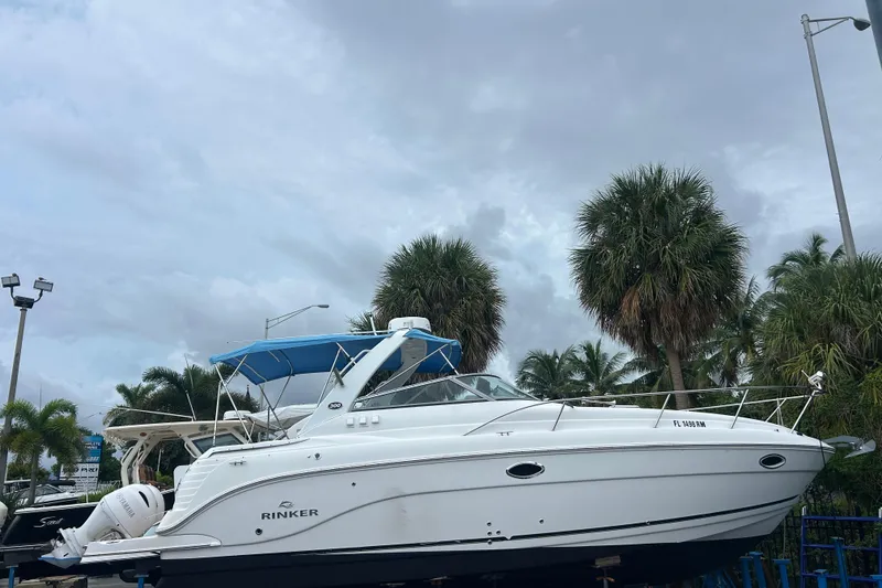 Slide: The Image of 2007 Rinker 300 Fiesta Vee boat with blue canopy, parked near palm trees. - 2