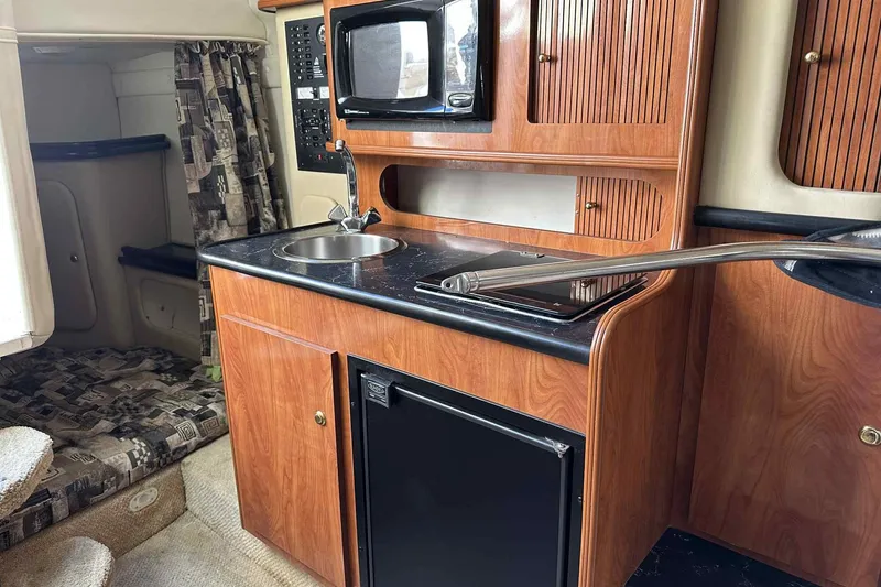 Slide: The Image of 2003 Rinker Fiesta Vee 290 boat interior with kitchenette, featuring wood cabinets and appliances. - 20